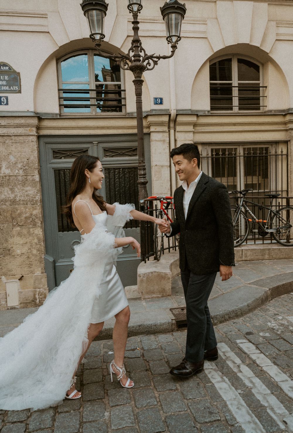 A couple shares a playful moment during their wedding photo session on a historic Parisian street corner.