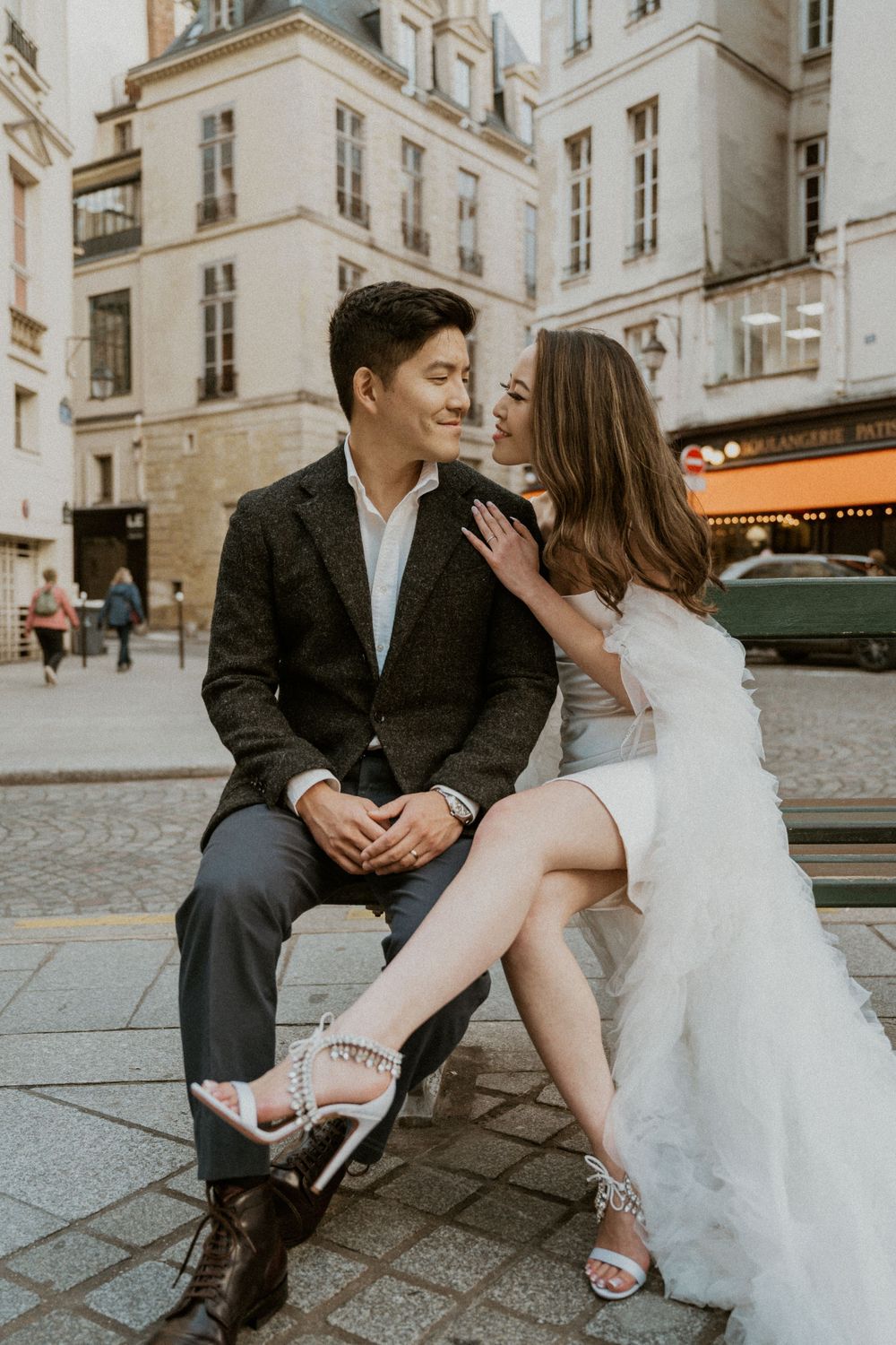 Romantic couple shares intimate moment on cobblestone street in Paris with elegant architecture in background.