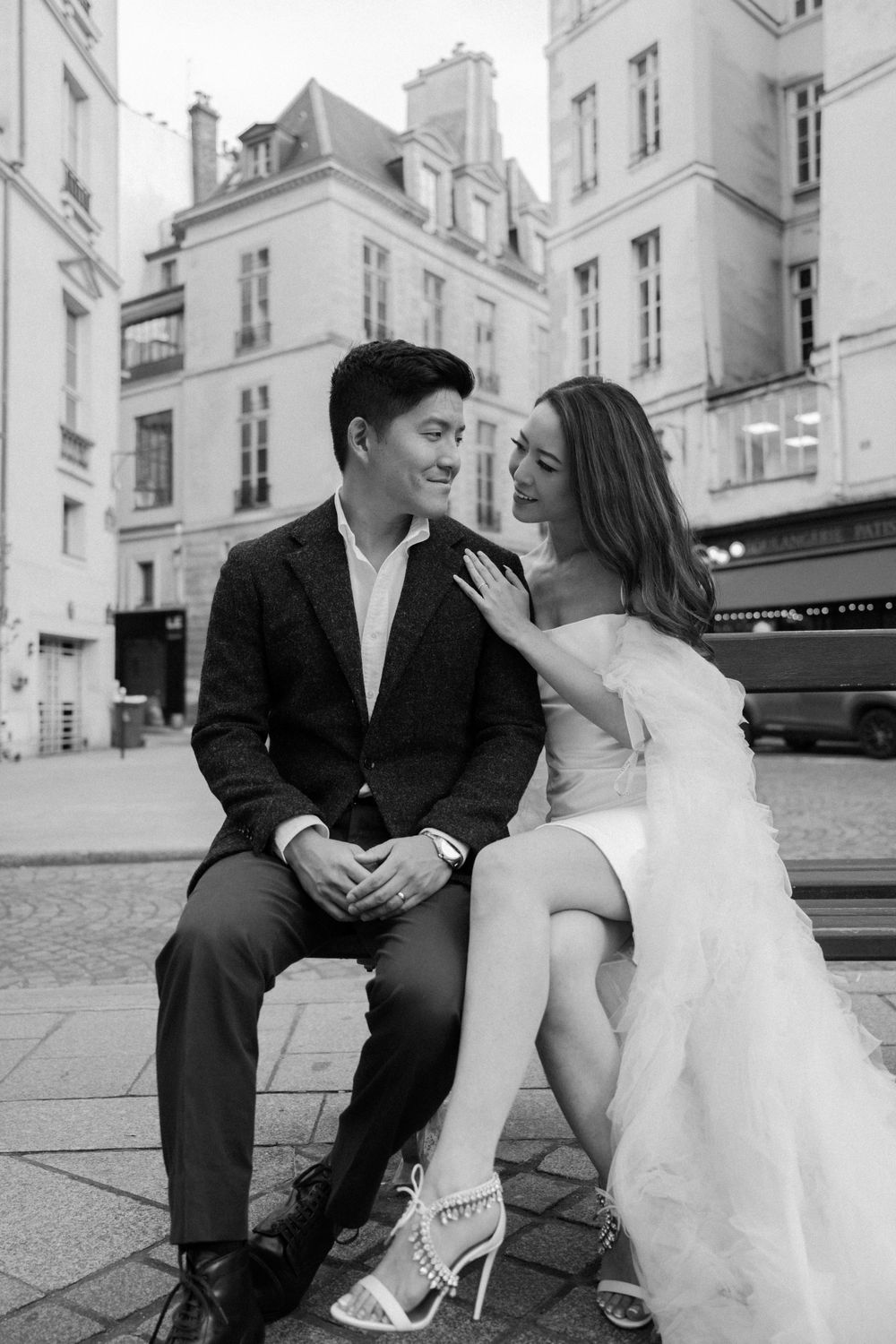 A black and white portrait of a couple sharing a joyful moment on a Parisian street corner.