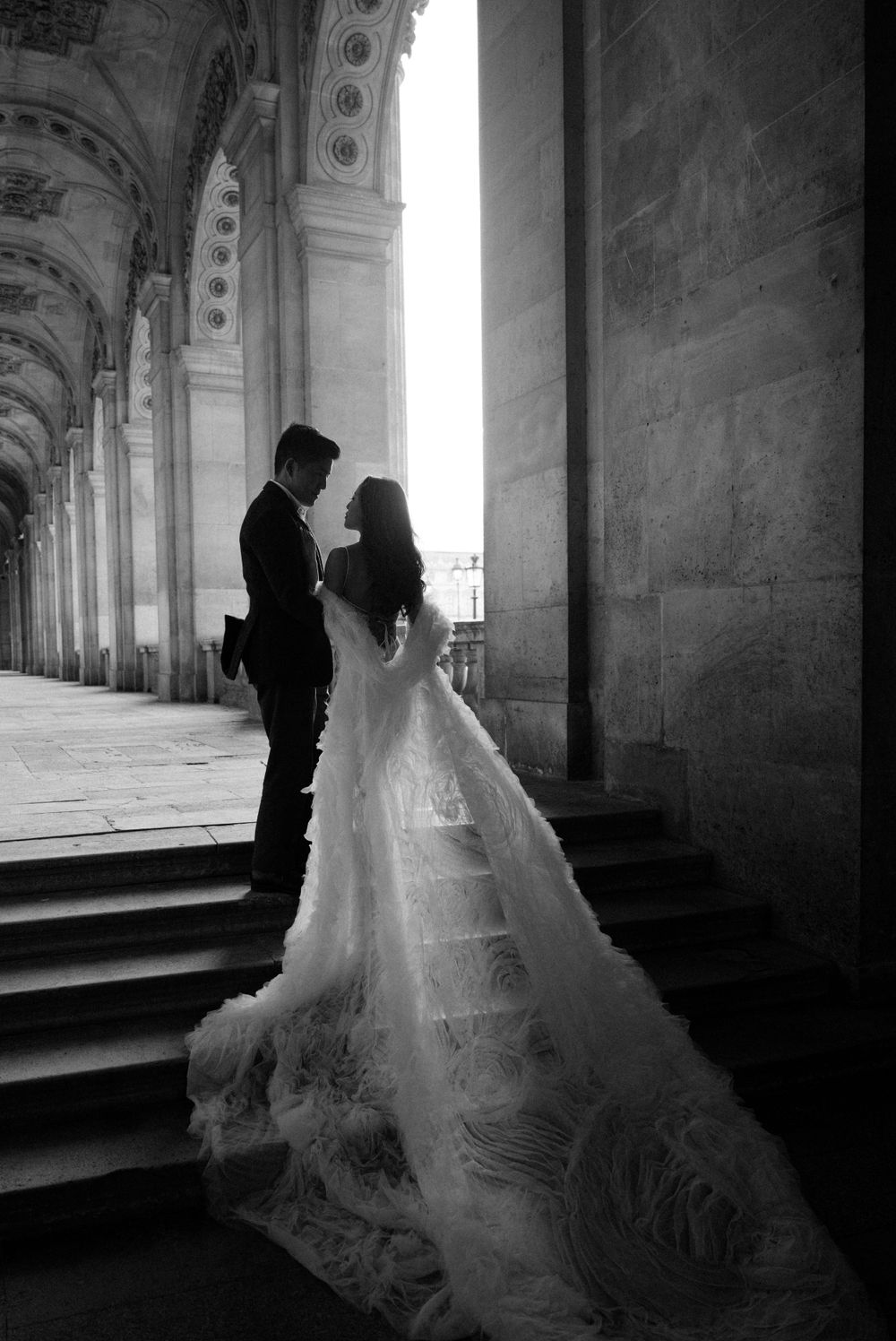 A romantic wedding photo silhouette under ornate stone arches with a flowing white dress trailing down stone steps.