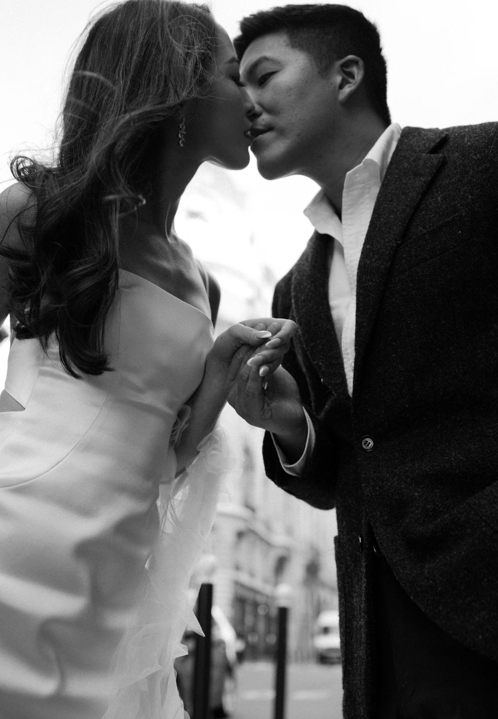 An intimate black and white portrait of a couple sharing a romantic moment against a blurred urban backdrop.