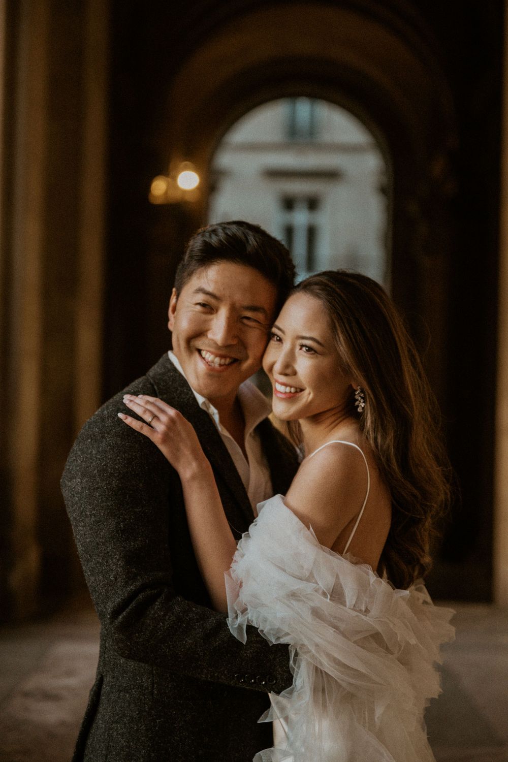 Intimate wedding portrait under stone archway with warm evening lighting.