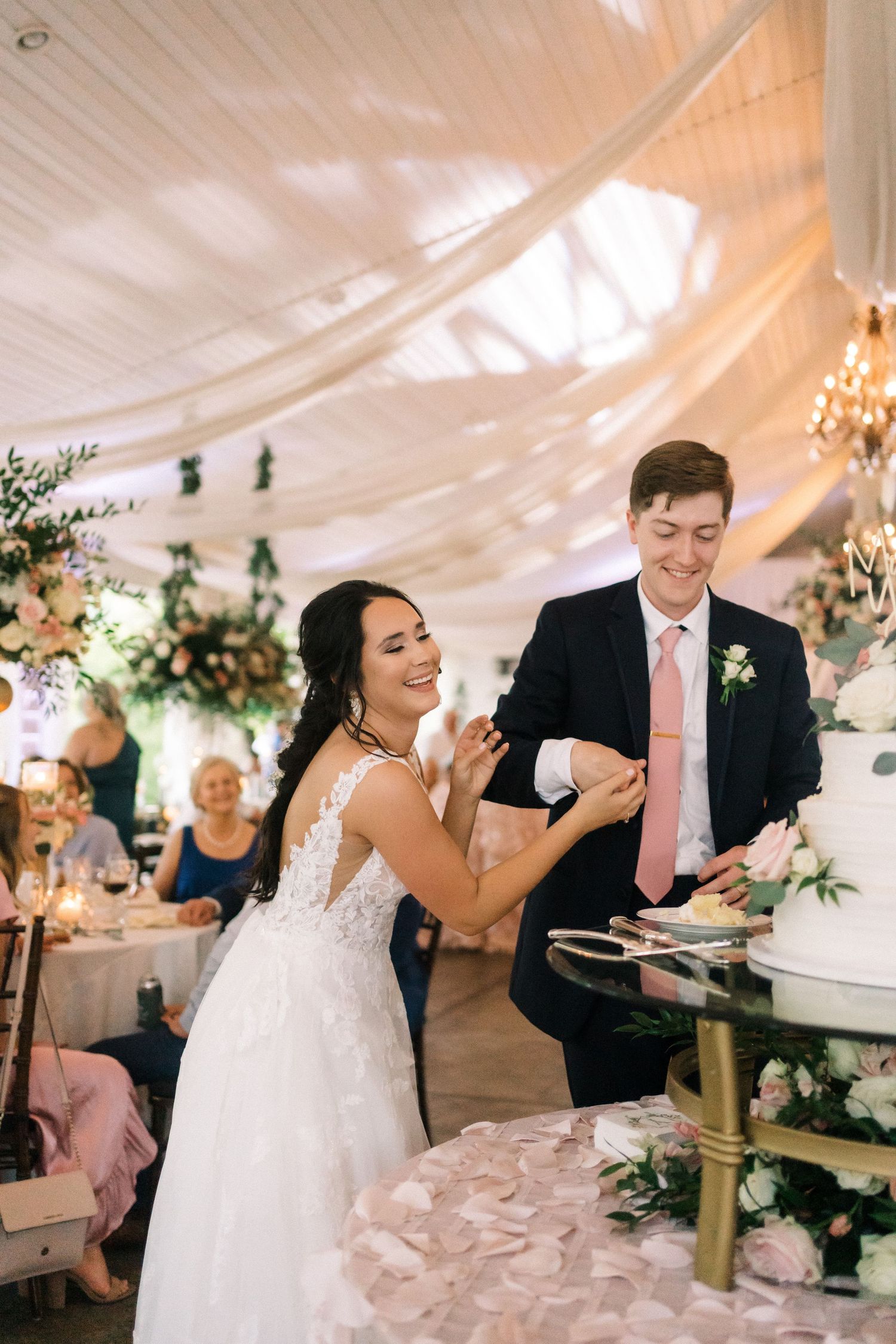 A playful cake cutting moment at a wedding reception under a white tent with floral decorations.