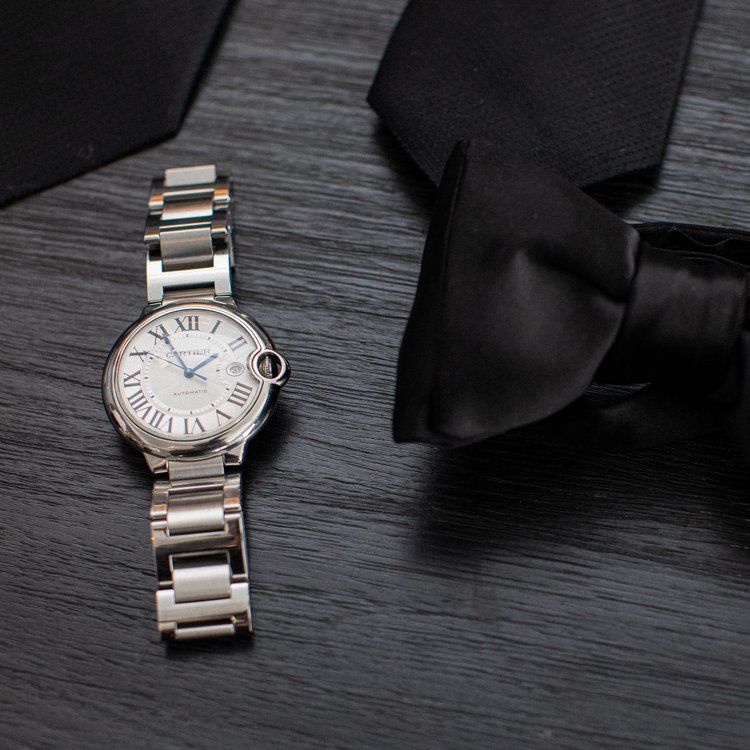 Silver and gold Cartier Ballon Bleu watch next to black bow tie on gray surface.