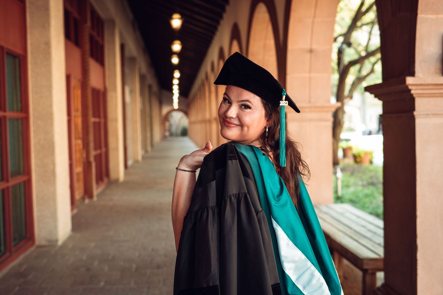 Graduate in cap and gown posing in an arched hallway.