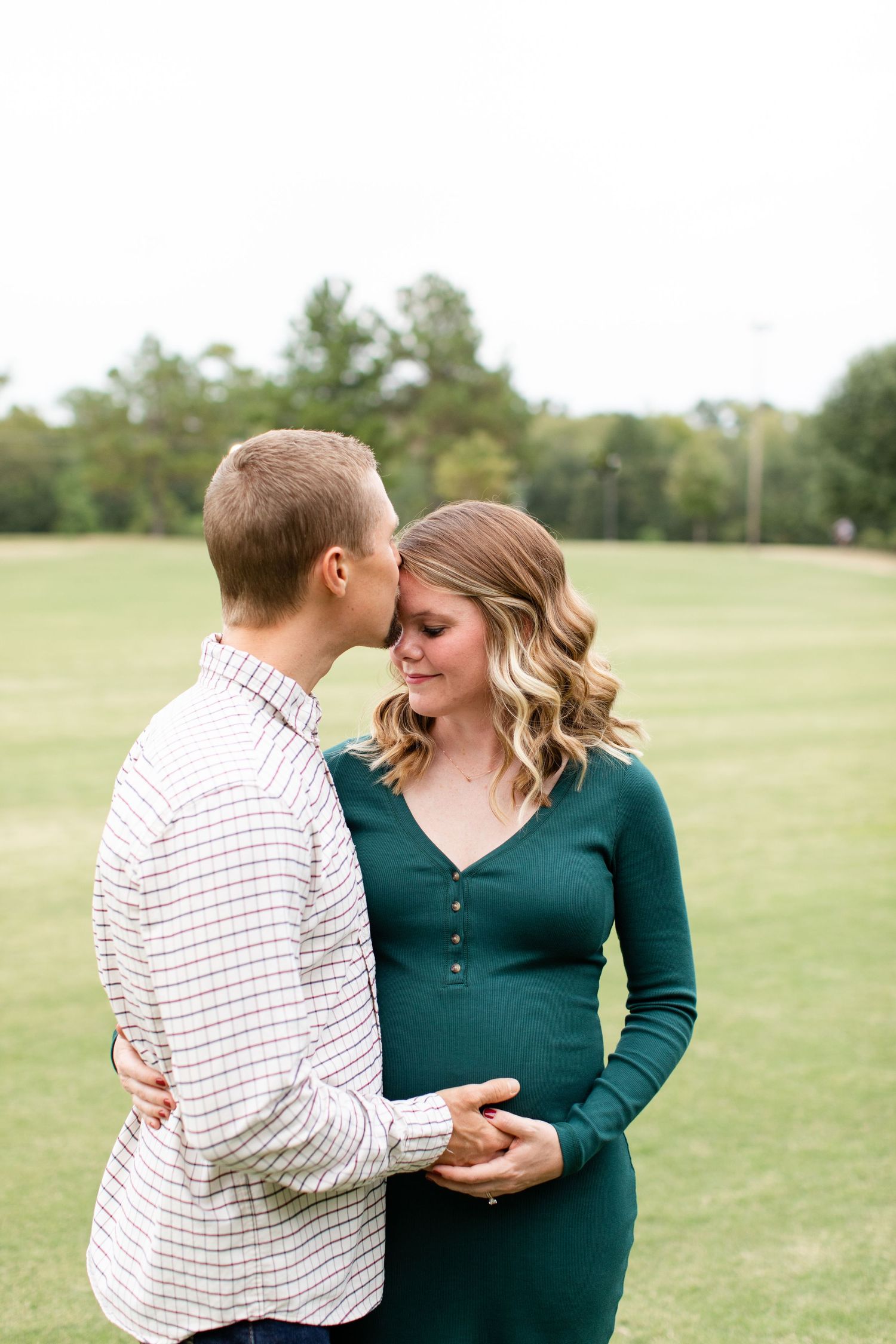 Intimate maternity portrait session in a grassy field with couple in coordinated casual attire.