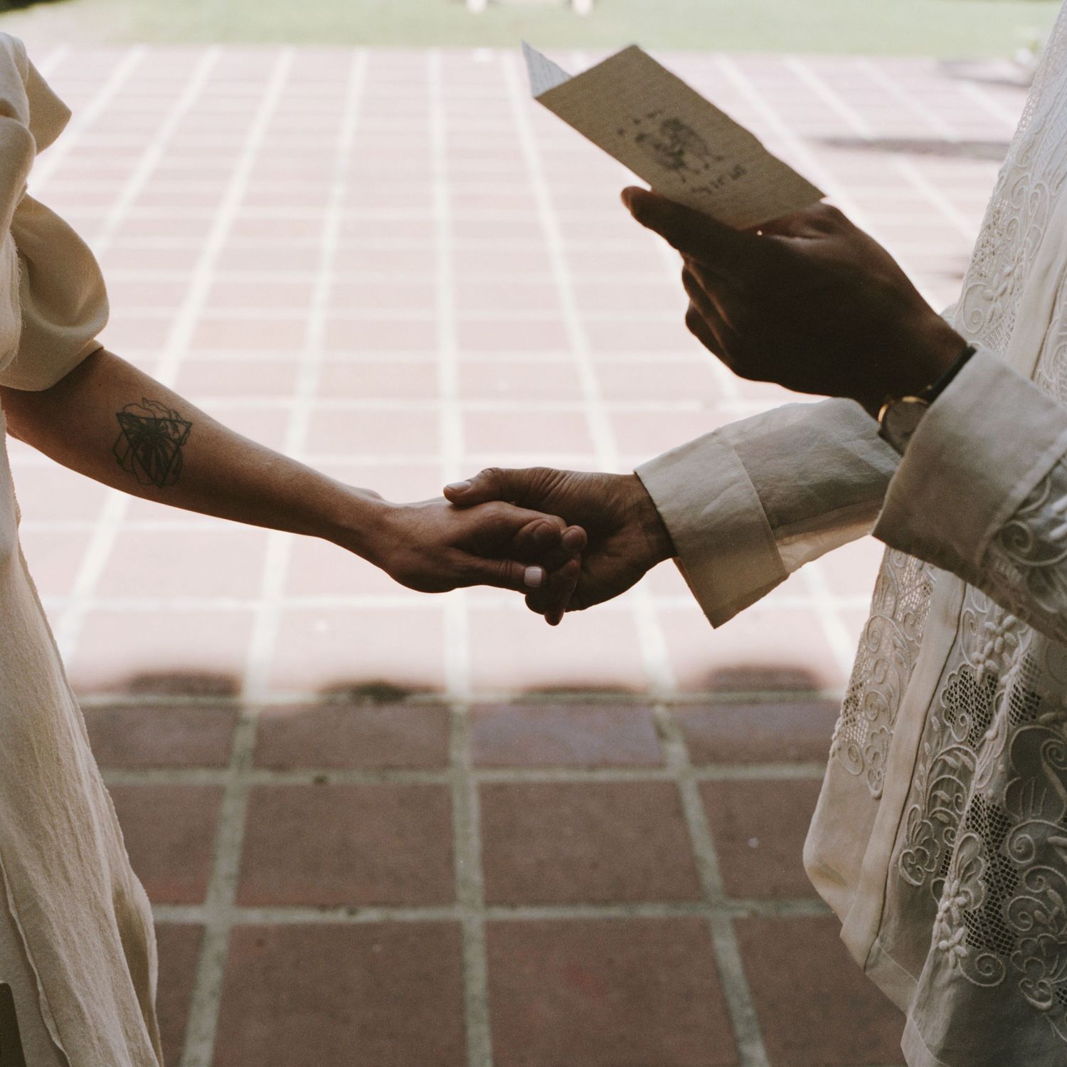 Close-up of hands exchanging wedding vows on a tiled courtyard.