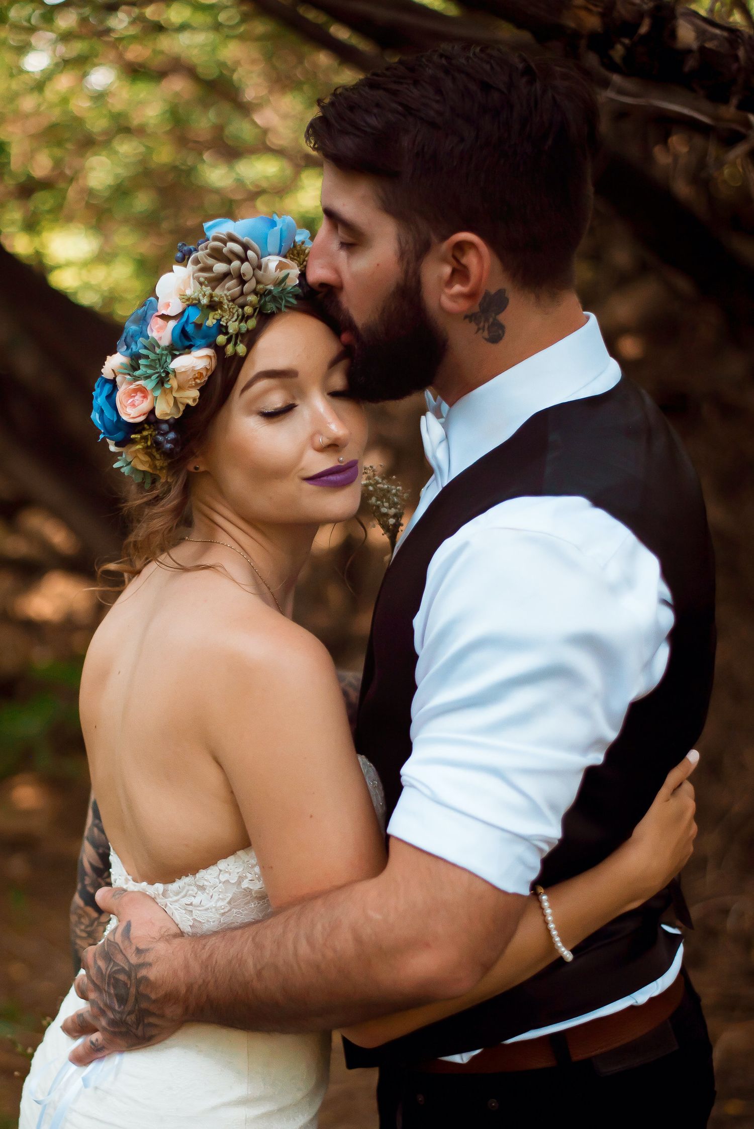 Romantic wedding portrait with floral crown and intimate embrace in natural setting.