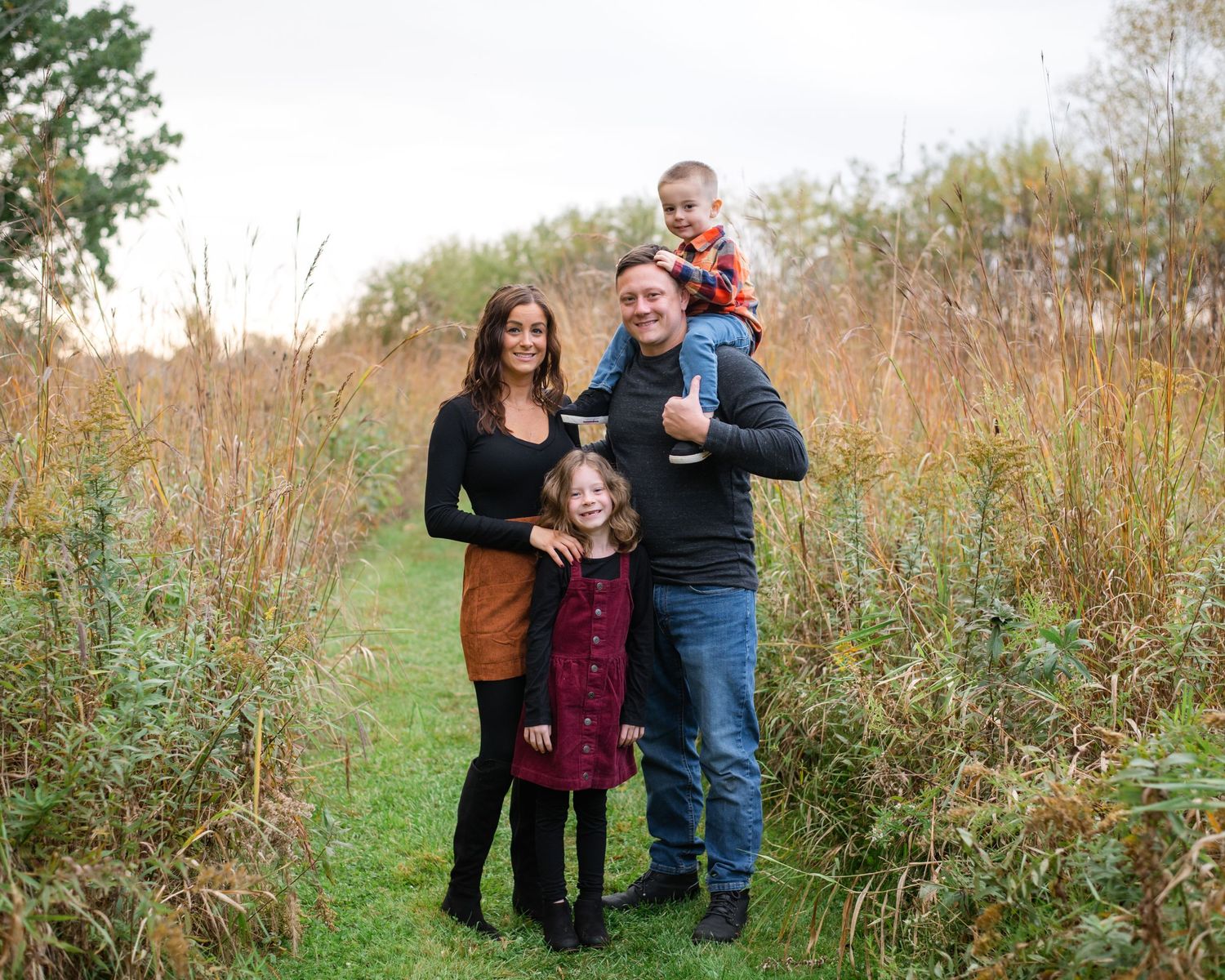 Family portrait in tall grass meadow during golden hour.