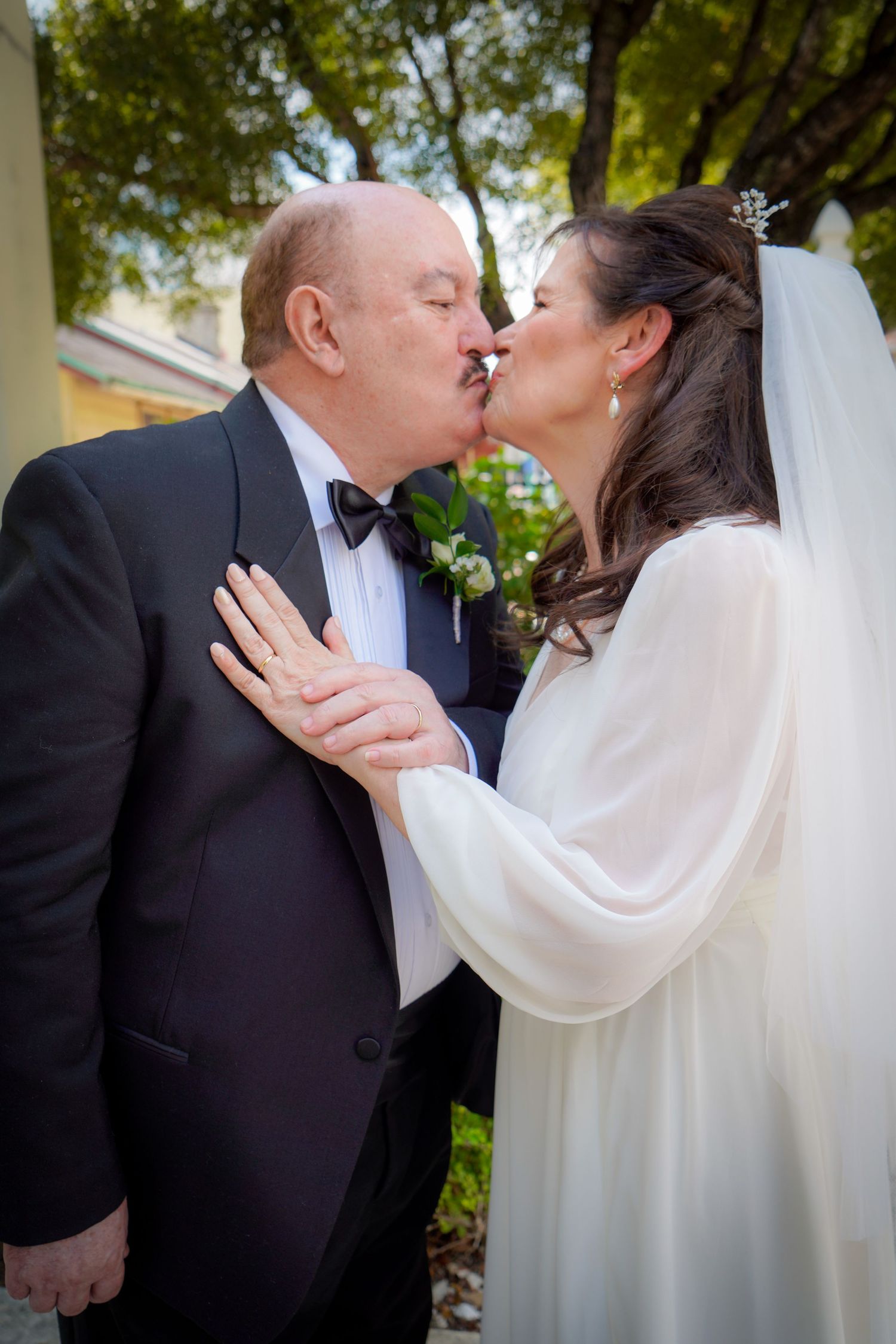 Bride and groom sharing a kiss outdoors, bride wearing veil and white gown with sheer wrap.