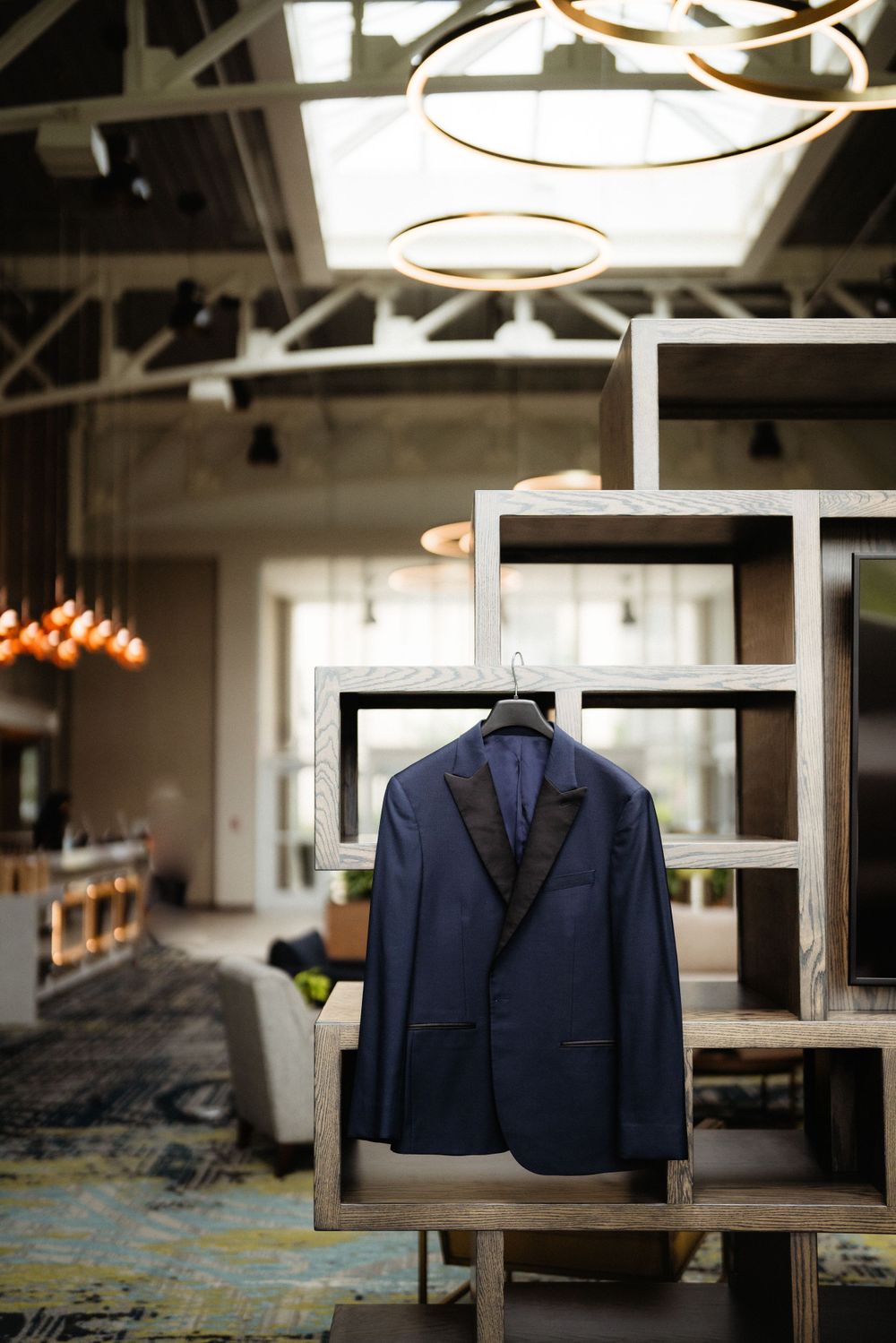 Navy blue suit jacket displayed on modern shelving unit under circular pendant lights.