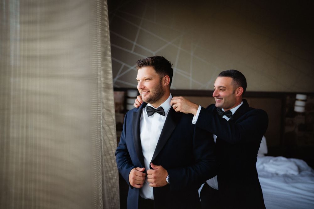Two people in formal suits share a joyful moment together in a hotel room.