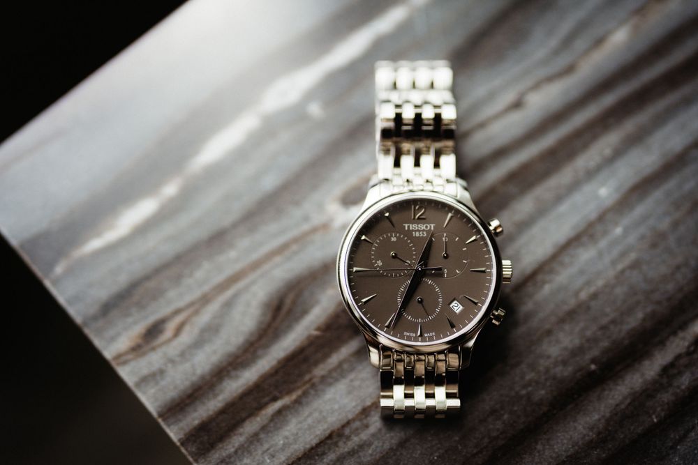 Silver chronograph watch with metal link bracelet on textured gray surface.