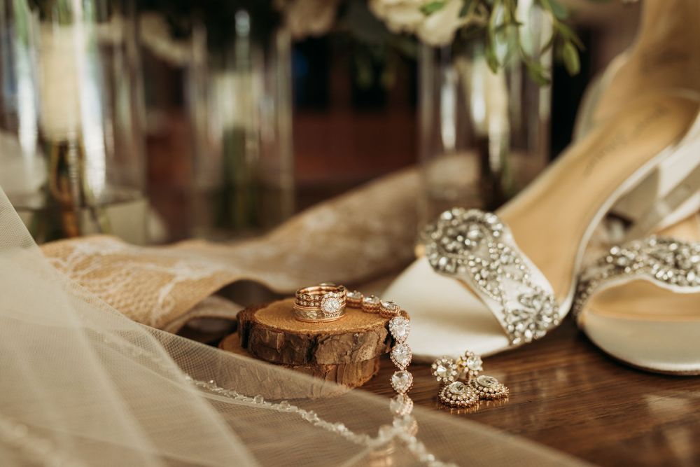 Wedding details featuring rings on wooden slice with elegant bridal shoes and lace.