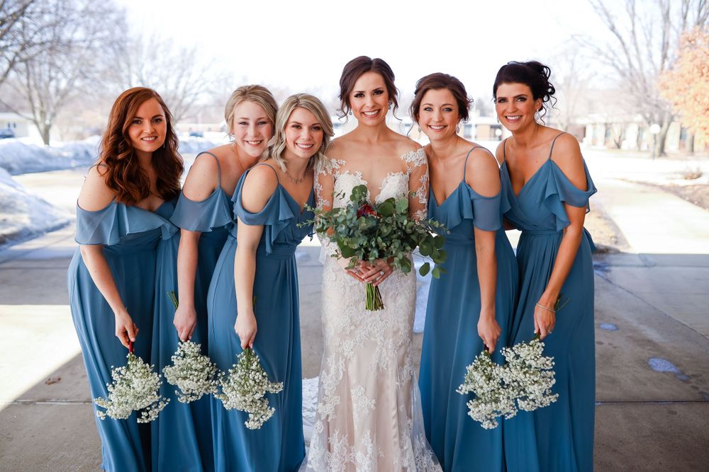 Wedding party in matching blue dresses holding winter bouquets outdoors.