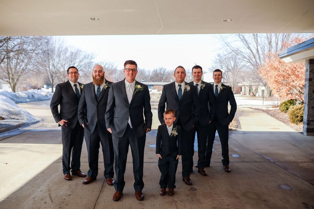 Groomsmen and young ring bearer posed together in formal attire against snowy backdrop.