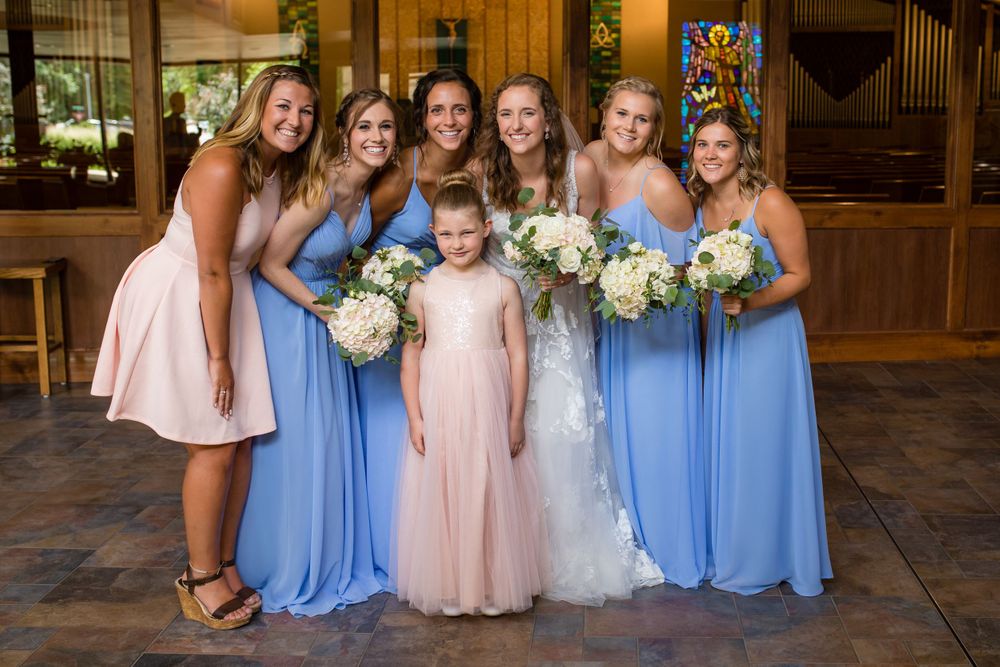 Wedding party posed together in blue and pink dresses holding white floral bouquets.