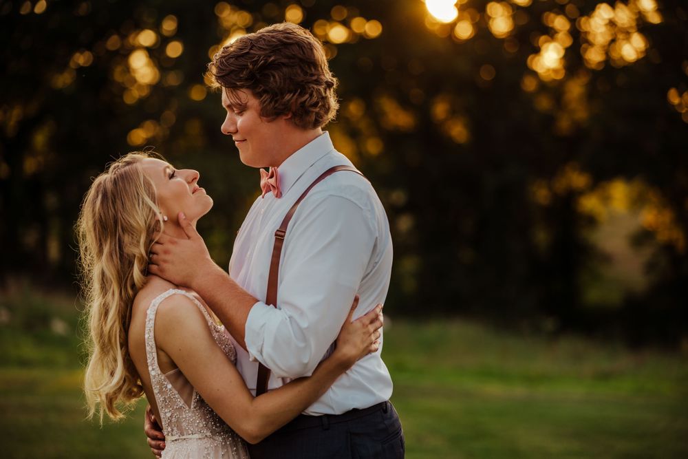 A romantic couple embrace during golden hour sunset in a grassy field.