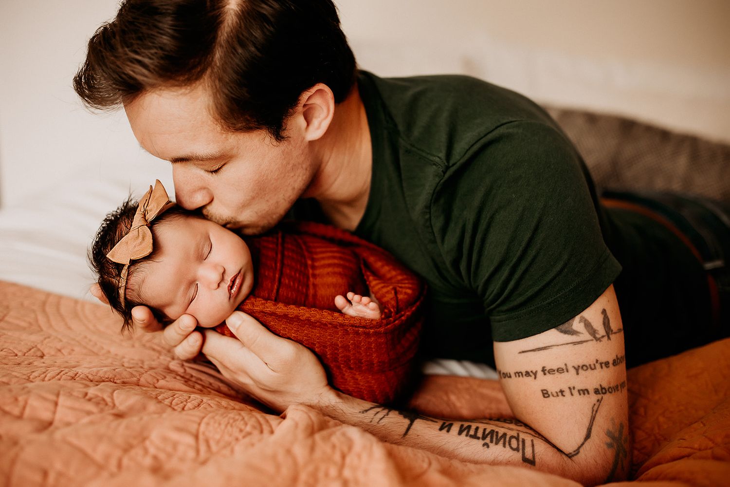 A father holds his bay girl in his arms while giving her a kiss on her temple.