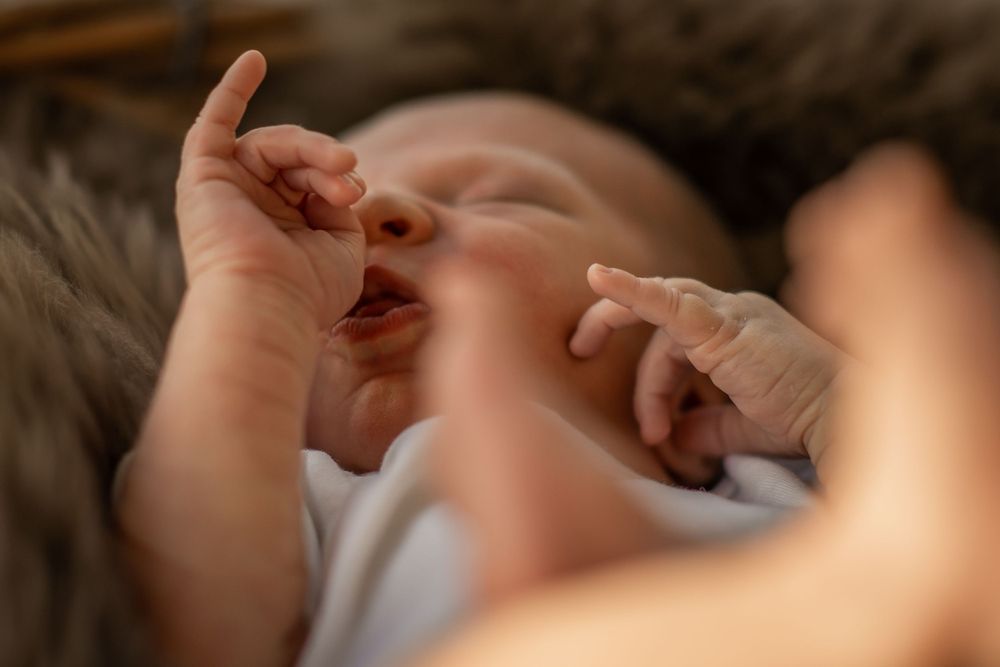 En søvnig baby i hvidt tøj ligger på en sløret overflade, mens den rækker op med deres små hænder.