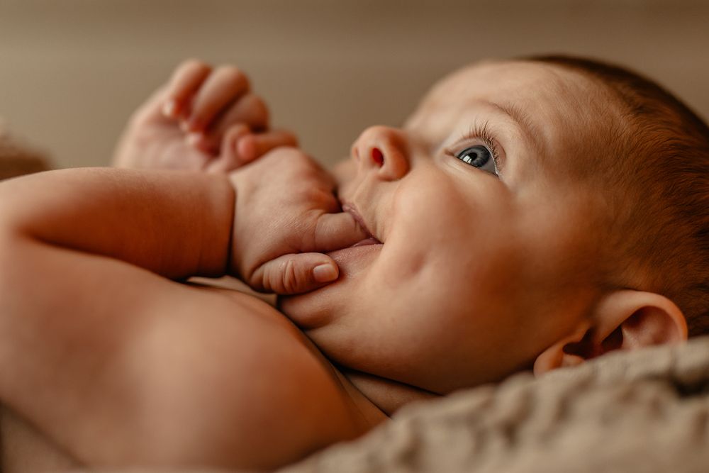 En baby, der ligger på ryggen i varmt lys med hånden tæt på munden, fanget i blødt fokus.