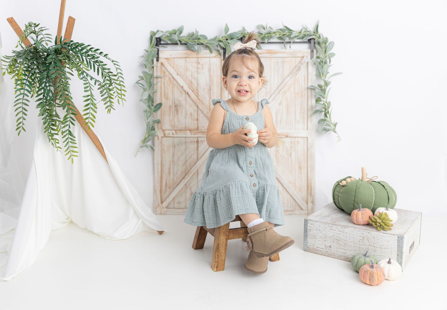 Studio photography setup with rustic barn doors, hanging plants, and fall decorative elements.