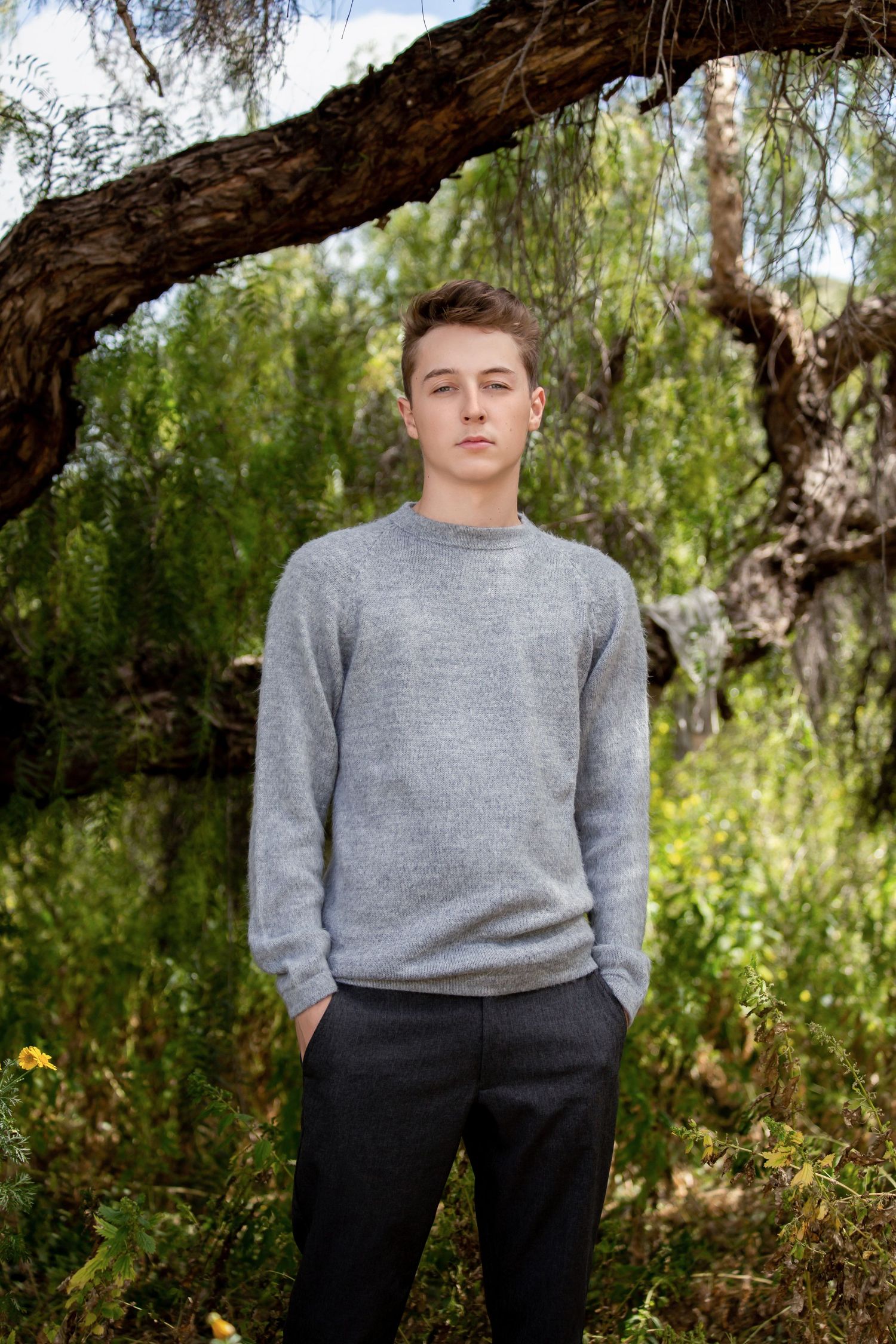 Casual outdoor portrait under willow tree branches in grey sweater.