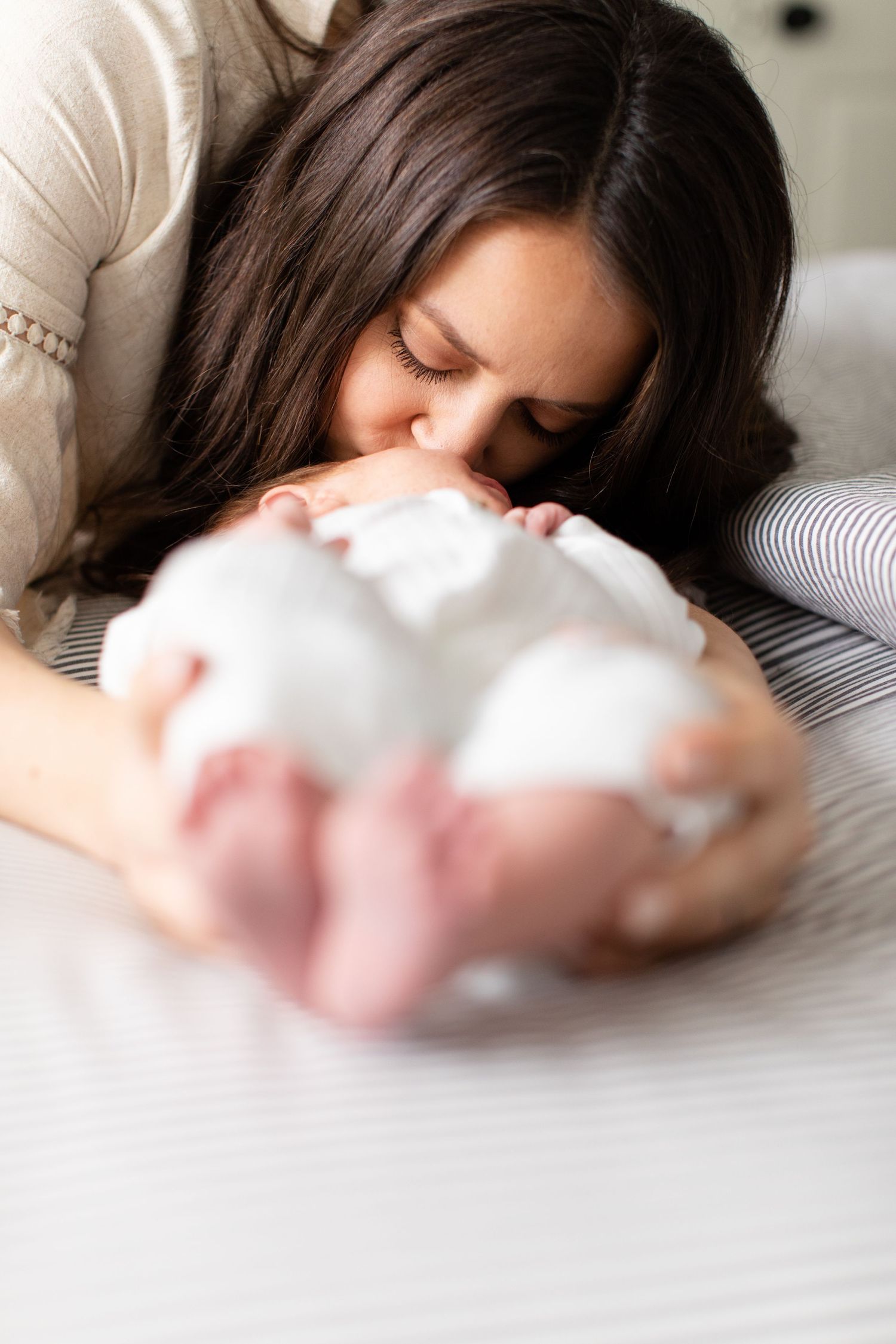 Intimate moment of parent giving baby gentle kiss while laying on striped bedding.