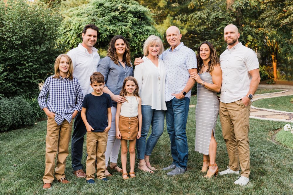 Extended family portrait outdoors with coordinated casual outfits in garden setting.
