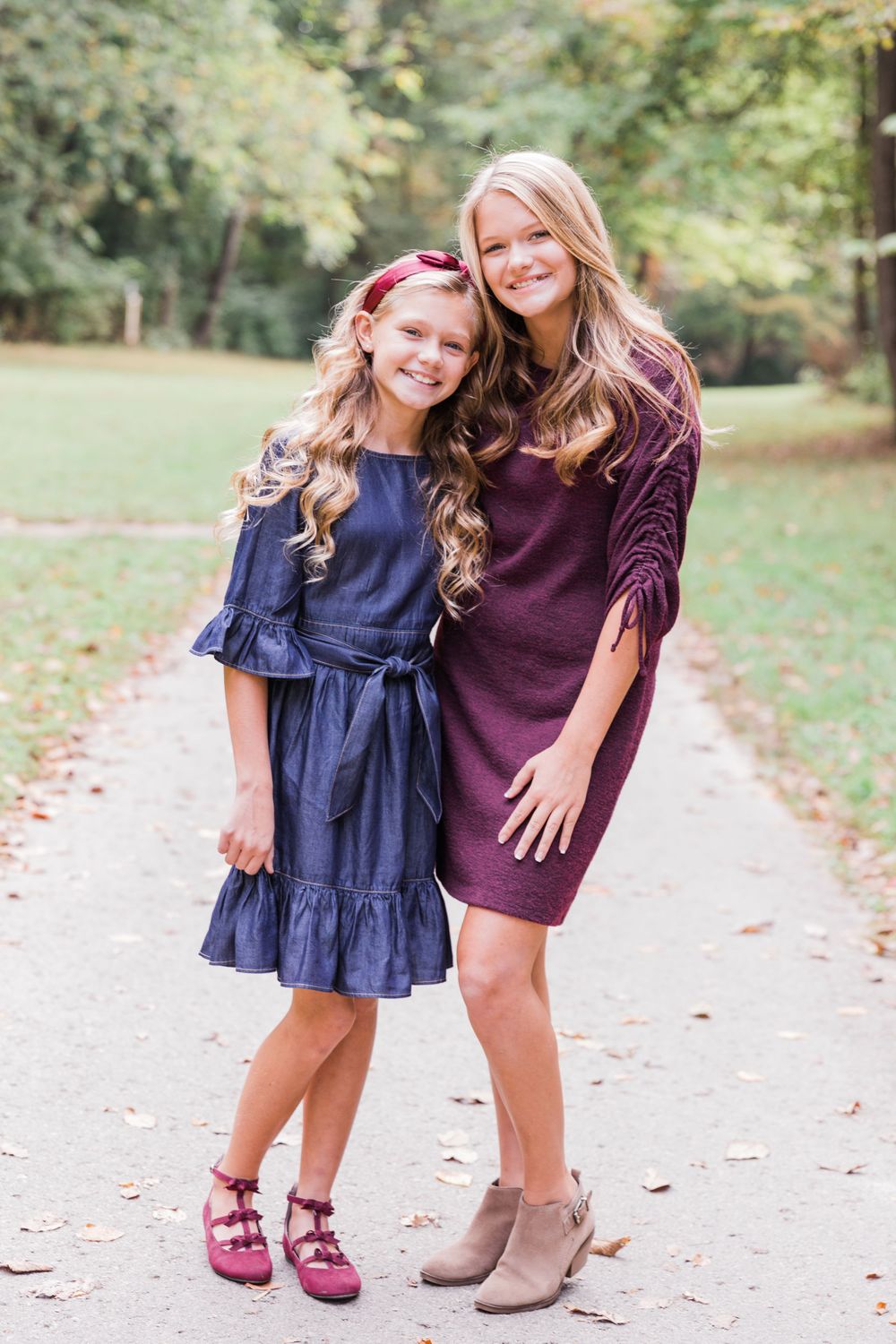 Two people in coordinating fall outfits standing together on a path in a park setting.