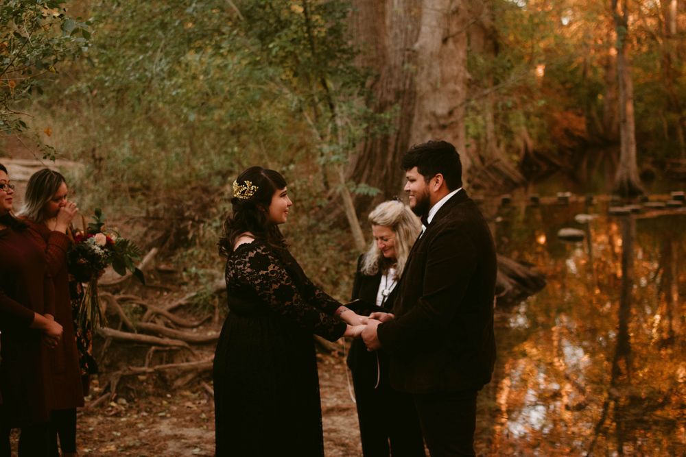 An outdoor wedding ceremony takes place in a golden-lit forest setting.