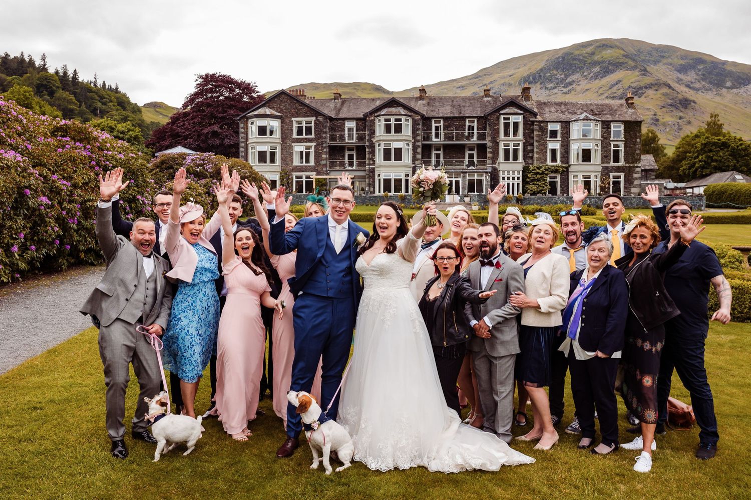 Cheerful wedding party with dogs poses in front of Scottish Highland lodge.