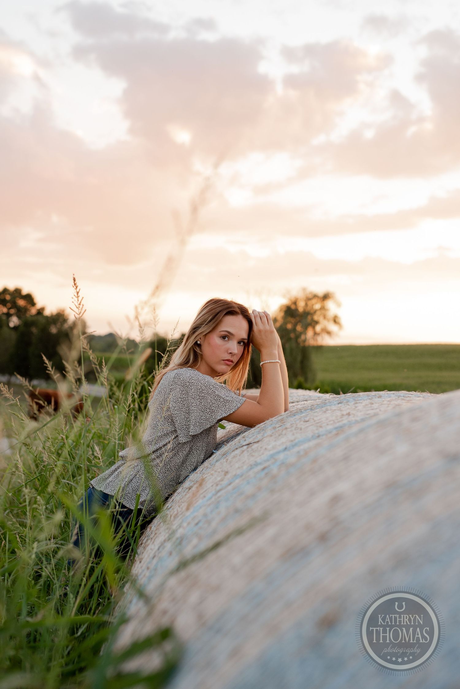 Artistic rural portrait against a large hay bale during golden hour.