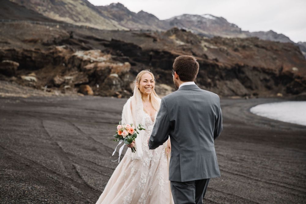 Wedding couple shares a moment on dramatic black sand beach with mountains in the background.