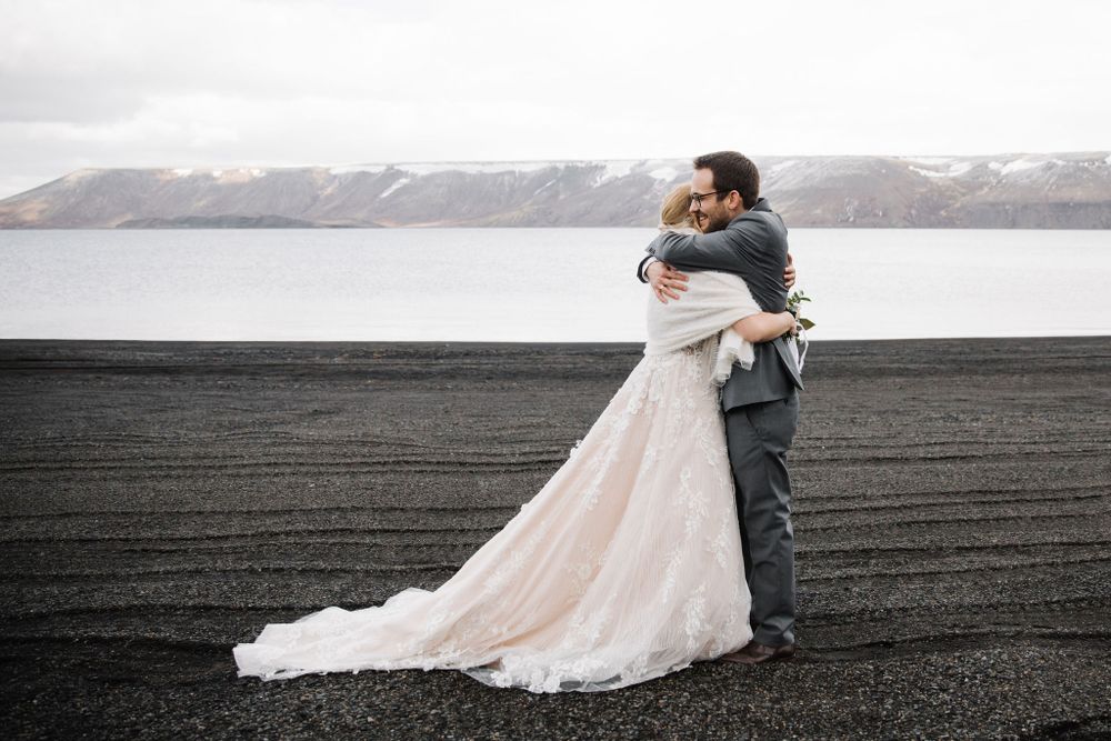 A romantic embrace between newlyweds on a volcanic black sand beach with mountains in the distance.
