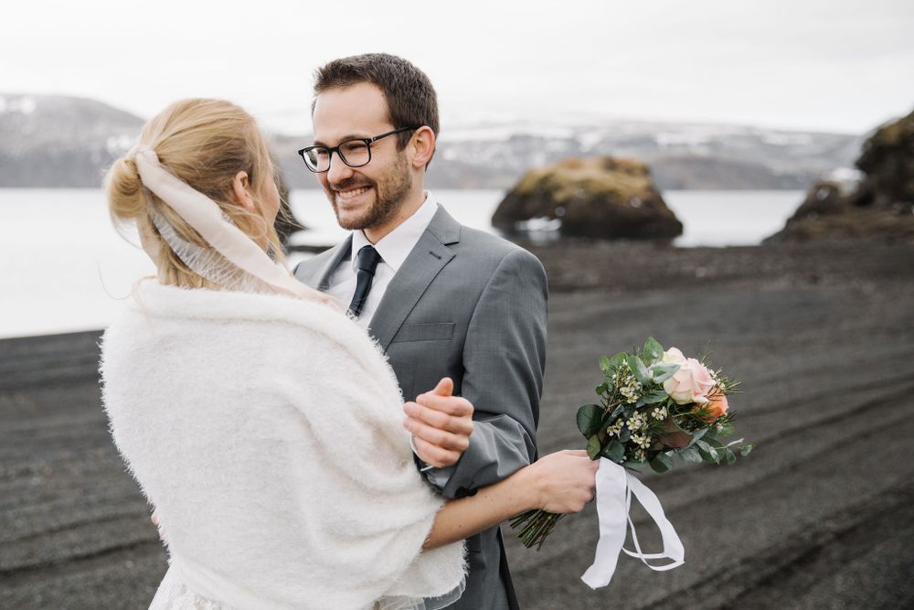 Intimate wedding moment on volcanic beach with mountain scenery.