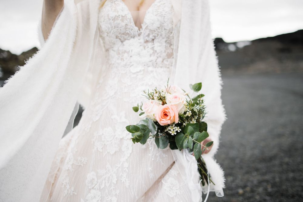 Close-up of a delicate bridal bouquet with pink roses against a lace wedding dress.