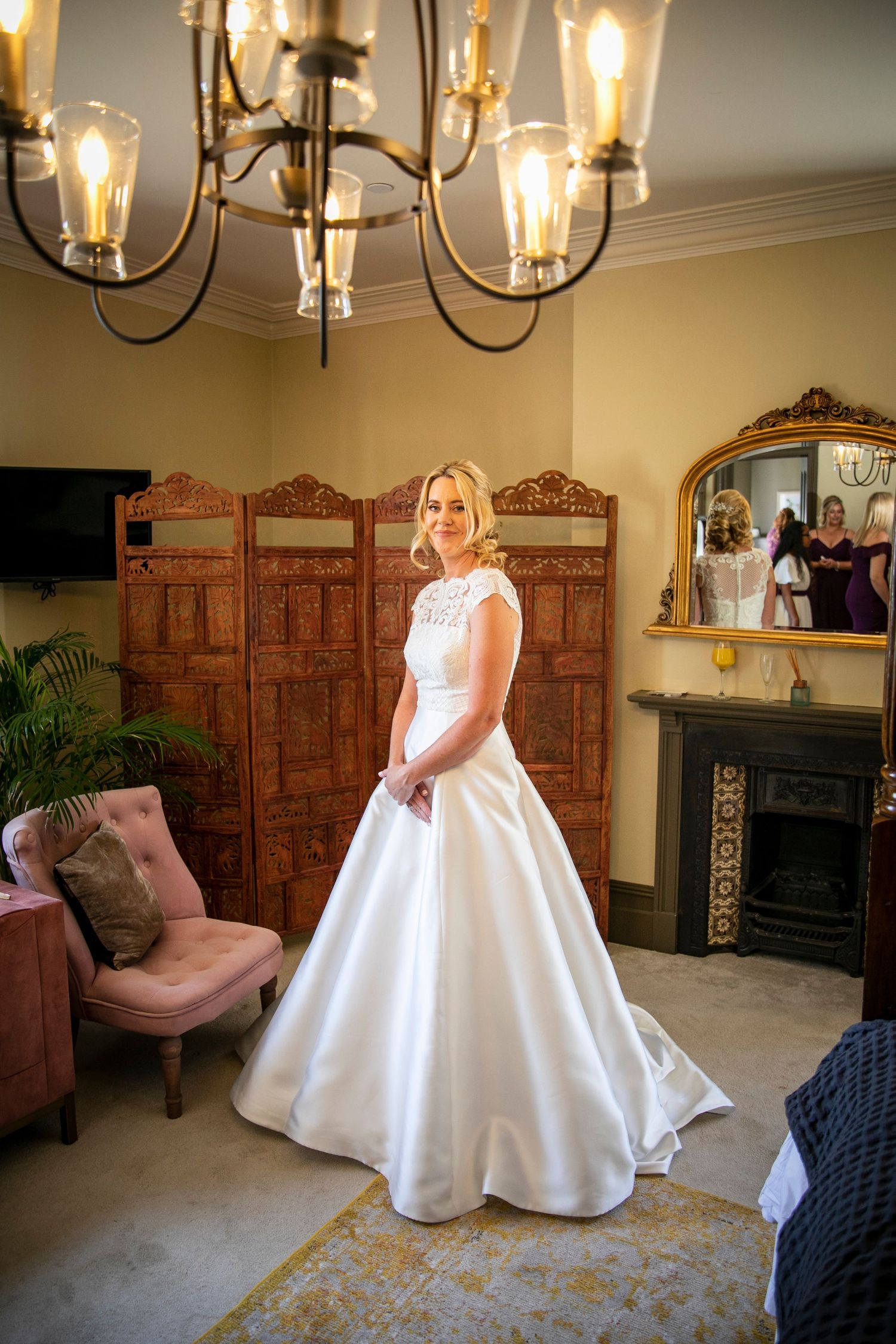 Elegant white wedding dress displayed in a room with vintage furniture and chandelier lighting.