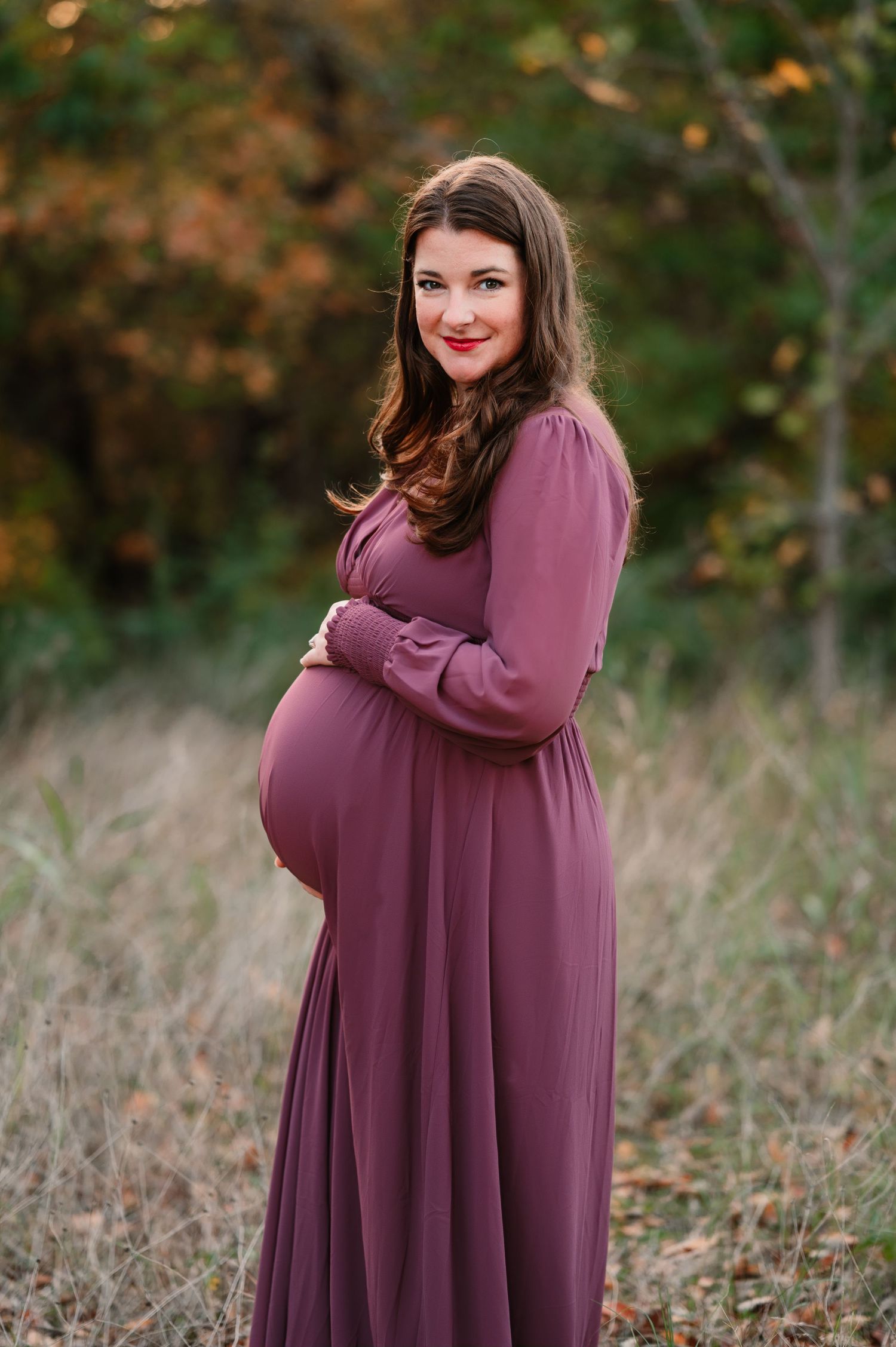 Mom smiling looking at camera holding baby bump during outdoor Dallas area maternity photo session at sunset