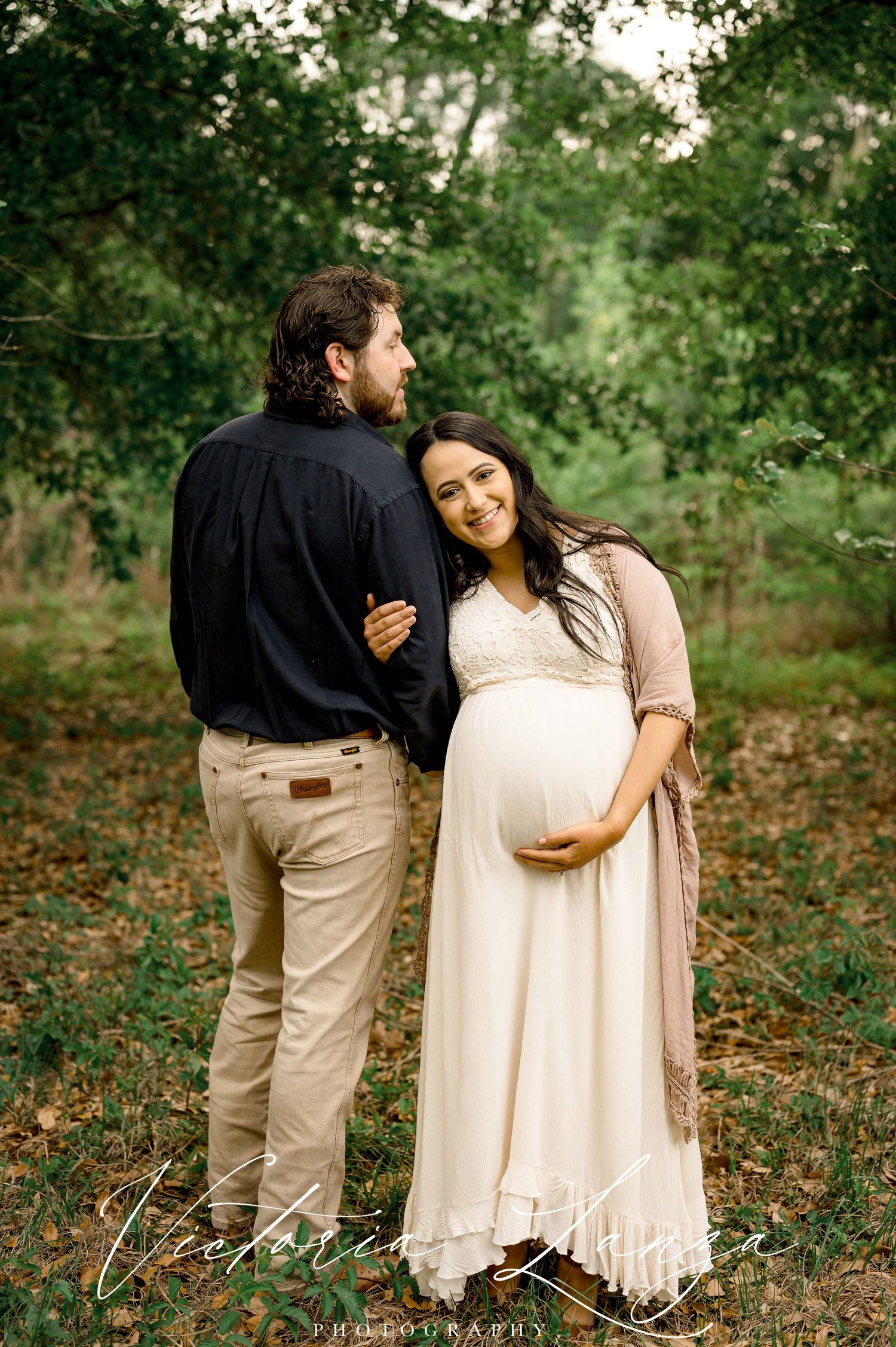 pregnant wife leaning on shoulder of husband surrounded by trees at memorial park in houston