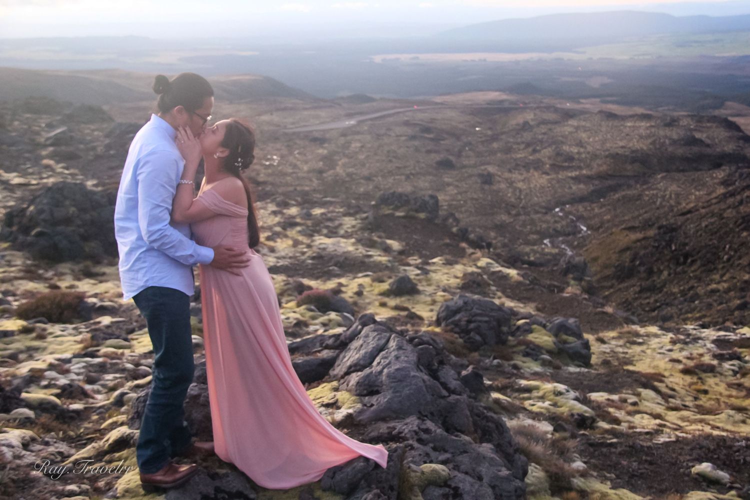 Couple standing on rocky mountain overlook with dramatic desert landscape view.