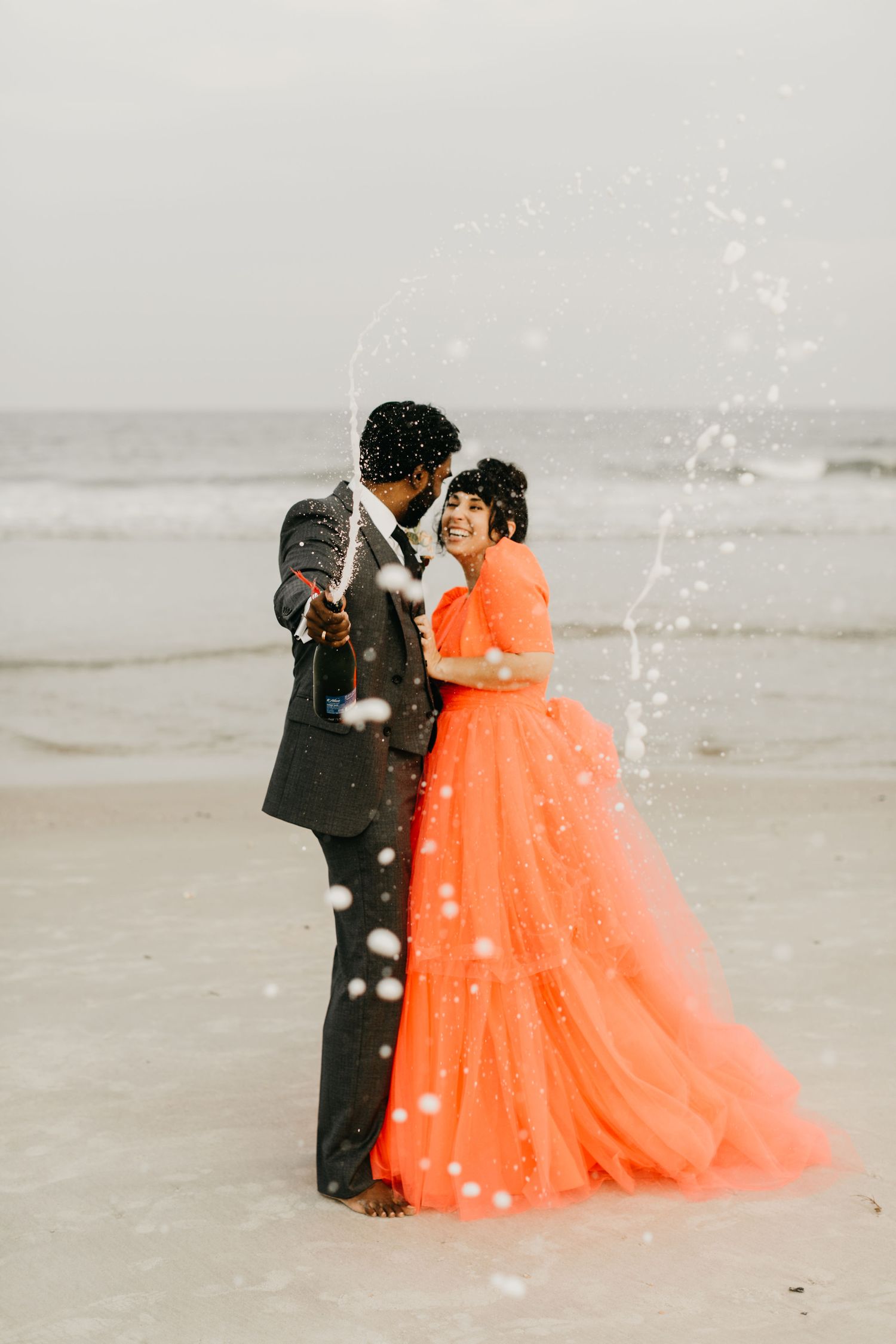 Couple in formal wear dancing on beach with orange ballgown and falling snow effect.