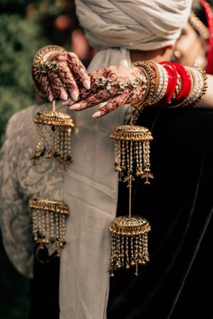 Detailed shot of traditional Indian bridal jewelry and henna adorned hands with gold kalire ornaments.