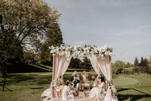 Outdoor wedding ceremony setup with pink draped arch and floral decorations in a garden setting.