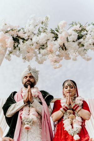 Traditional Sikh wedding couple praying under floral decor during their ceremony.