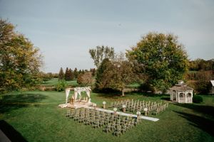 Elegant outdoor wedding setup with white chairs and gazebo in a lush garden setting.