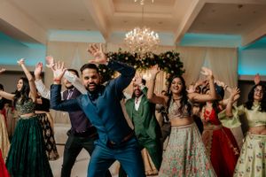 Energetic dance celebration with guests in colorful traditional attire at Indian wedding.