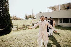 Wedding guest in cream-colored outfit dancing joyfully on sunny outdoor lawn.