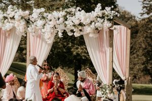 Traditional Indian wedding ceremony under floral mandap with pink drapes and white flowers.
