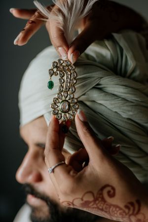 An ornate jeweled turban accessory being carefully placed during wedding preparations.